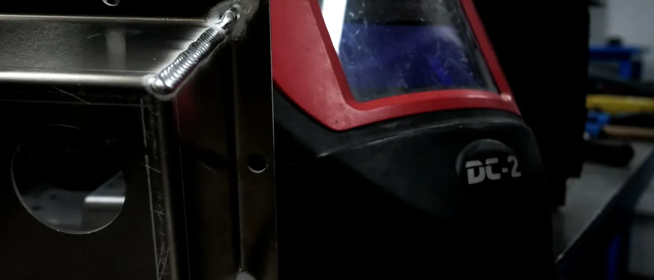 Conjunto soldado en aluminio junto a una careta de soldadura
